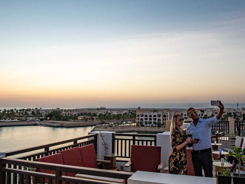 A couple at the horizon rooftop bar taking a selfie with the sea and the sunset at Hawana Salalah Oman