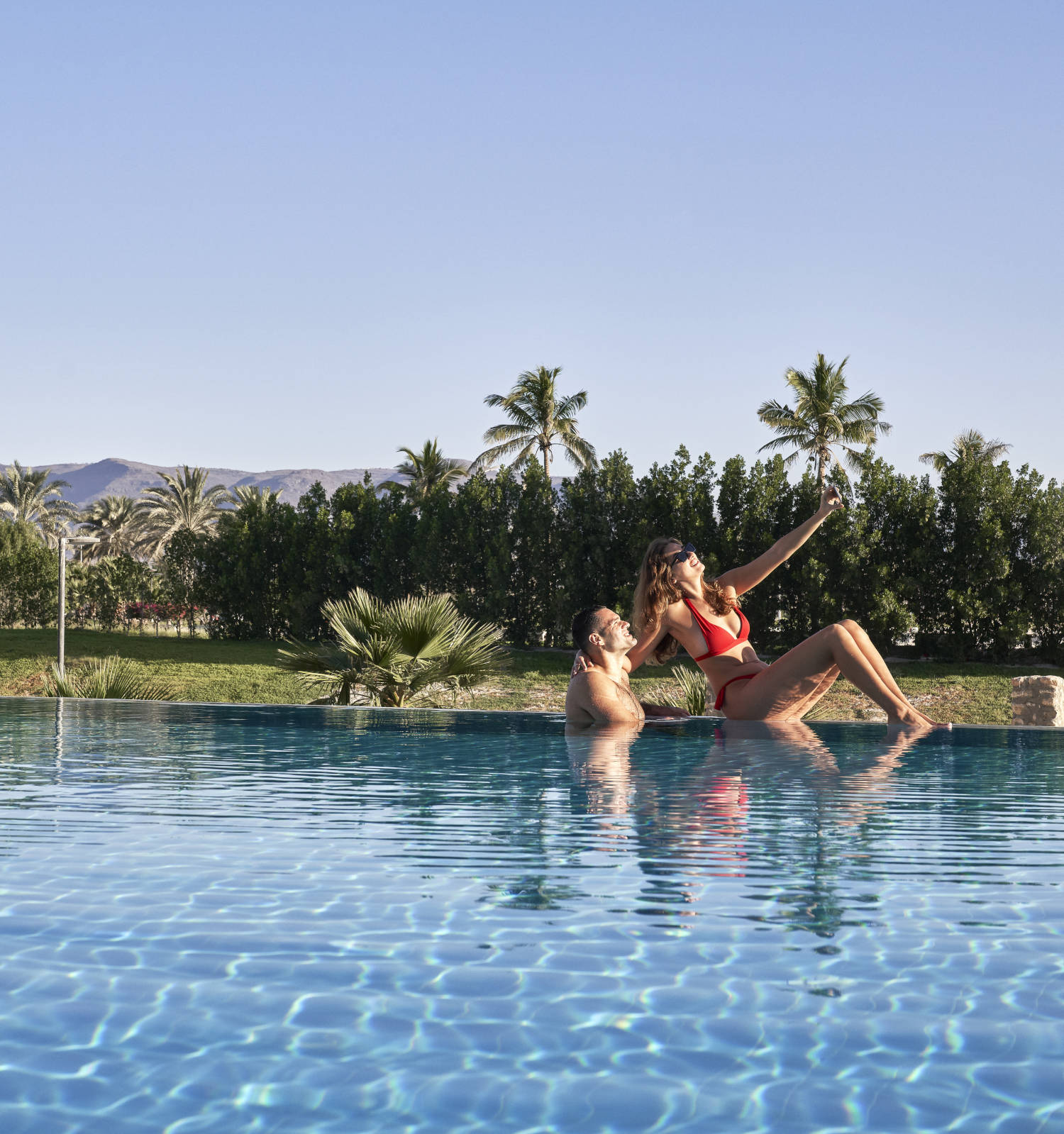 couples taking a selfie by the pool during the day inside fanar hotel and residences in hawana salalah