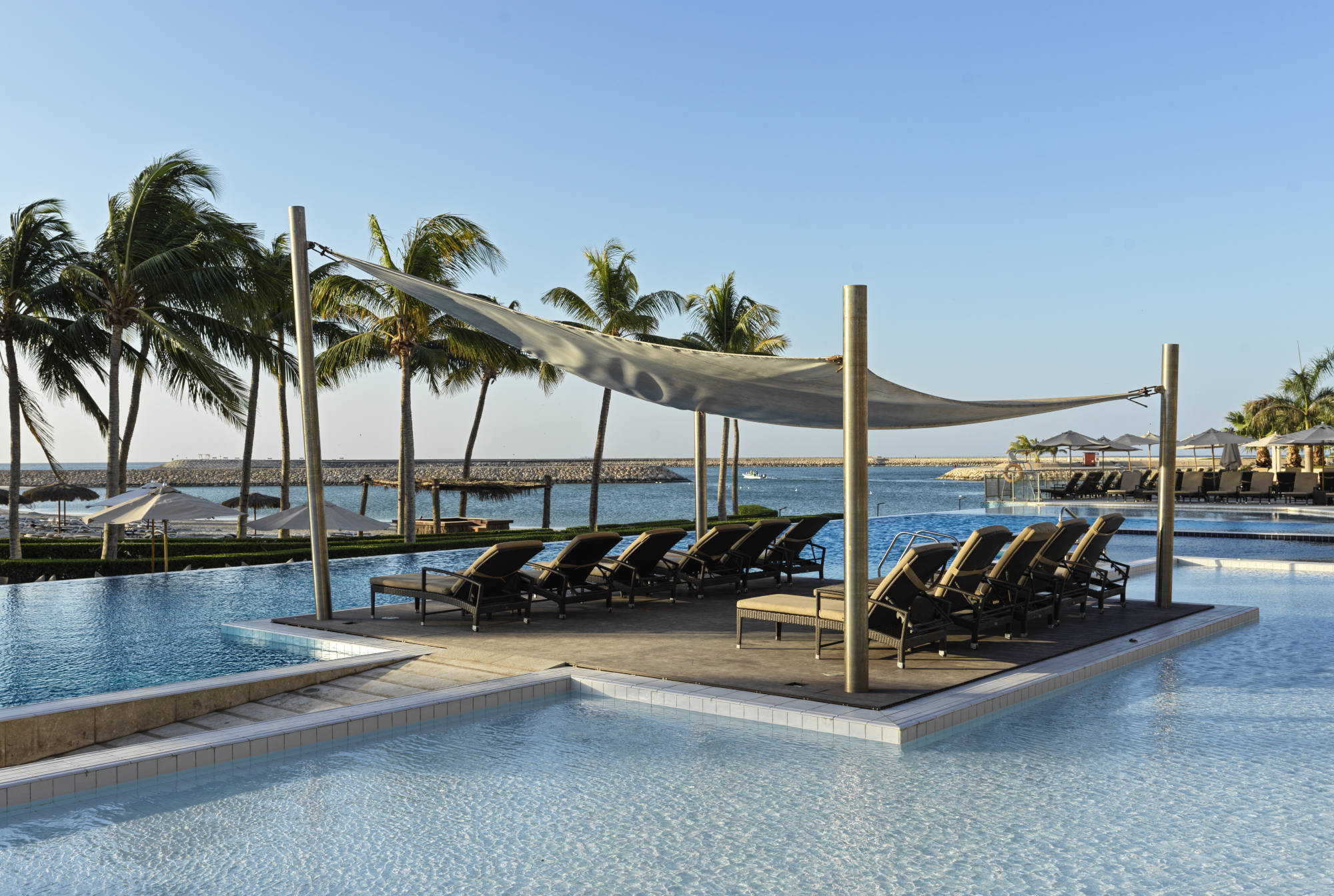 pool area with seating decks and arabian sea infront of it inside fanar hotel hawana salalah 