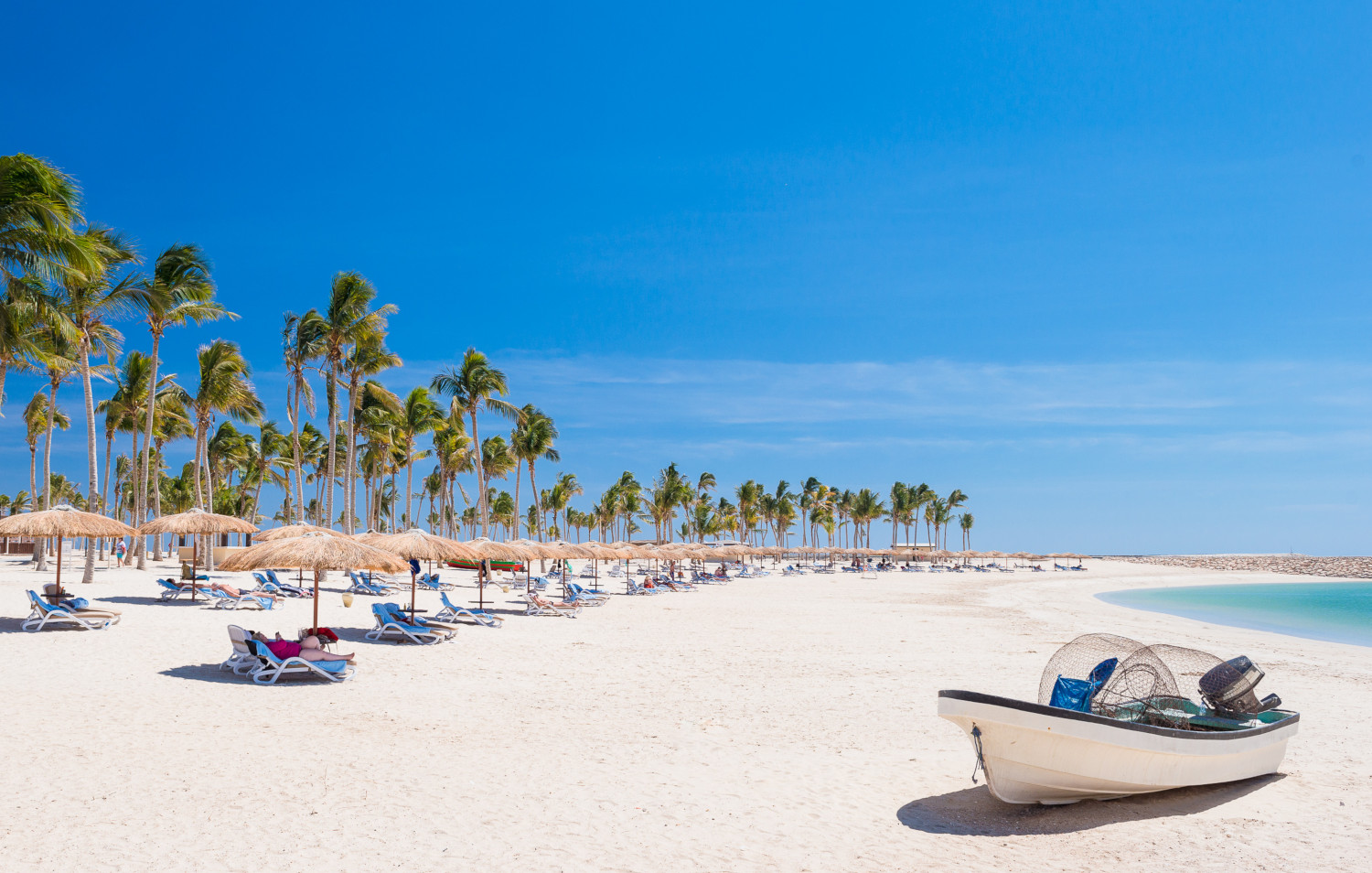 small boat infront of beach seating area and decks with sun beds at hawana salalah beach 