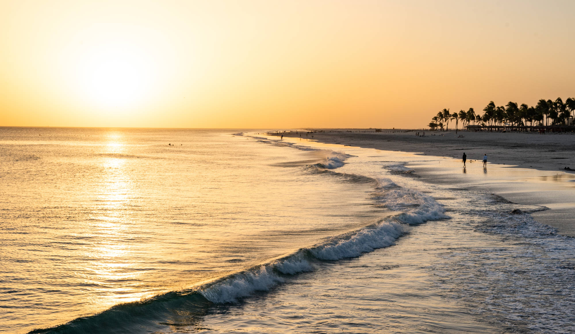 the sunset over arabian sea and hawana salalah beach with couples walking by the beach 