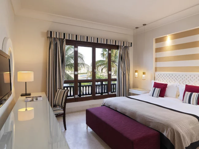 a double bed with a chair and desk by the balcony in a two bedroom apartment at fanar resort in hawana salalah oman