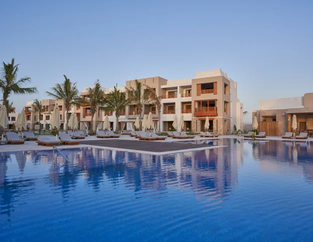 The Club by Fanar pool and building view, palm trees and sunbeds around the pool.