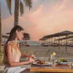 A girl having dinner with a sea view at The Club By Fanar Hotel